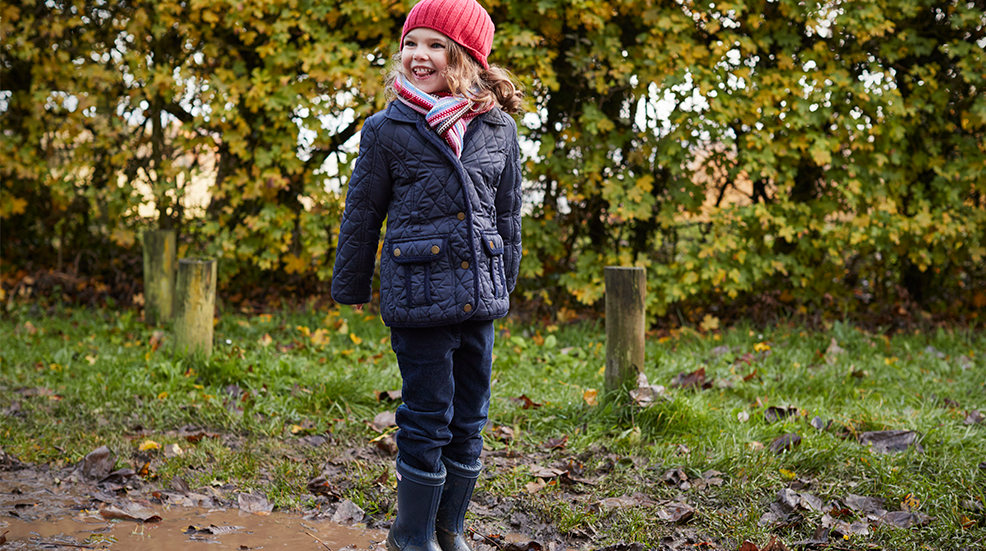 A young girl splashing in a muddy puddle